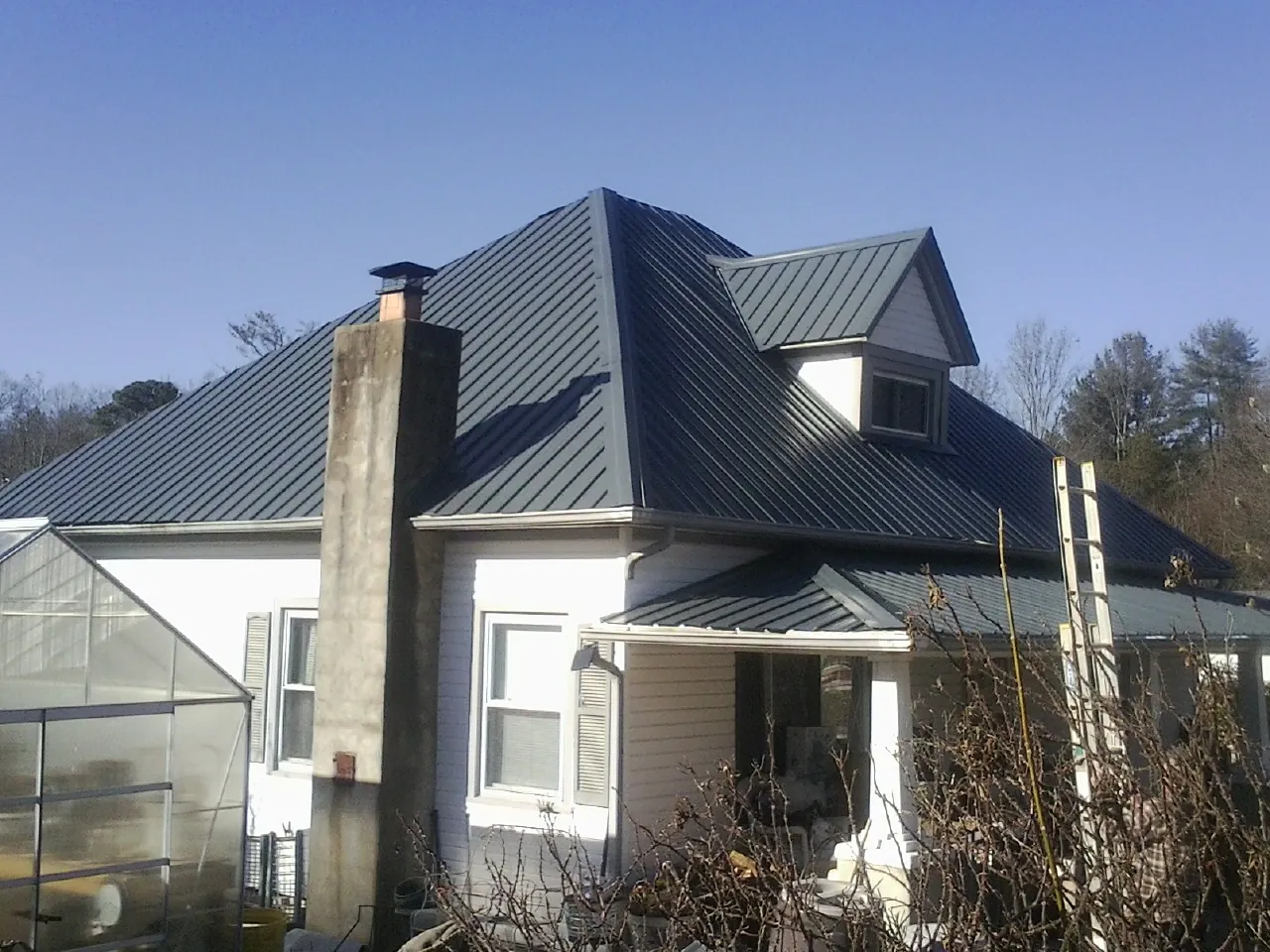Dark blue standing seam metal roof on a white farmhouse with dormer — Slate & Tile Roof Repair by Roofing Brothers in Lone Wolf