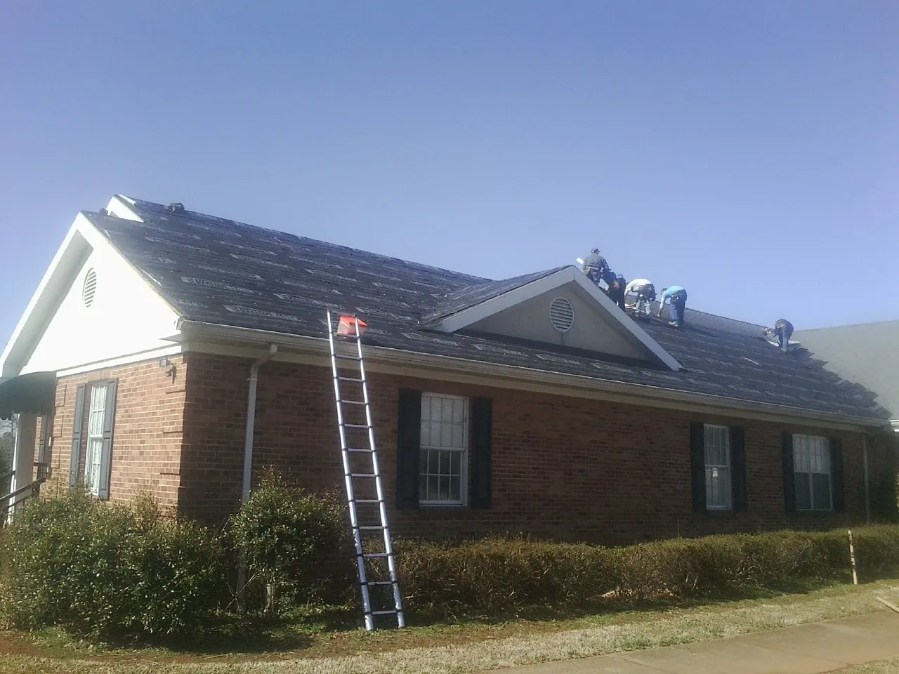 Crew tearing shingles off a brick ranch roof with a ladder set — Emergency Roof Repair work by our crew in Lone Wolf