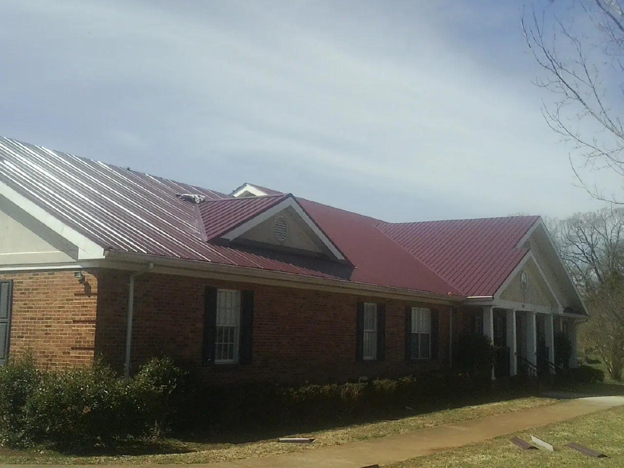Red metal roof with gabled entries on a long brick building, from a Hail Damage Roof Repair job in Lone Wolf