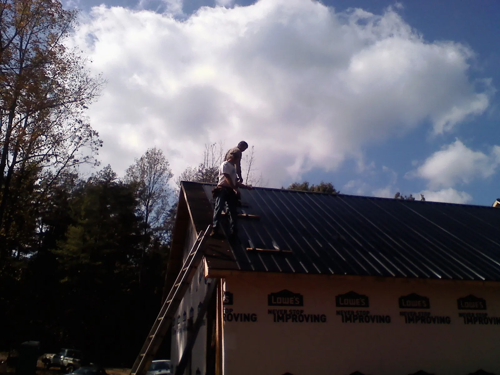 Roofer fastening dark metal panels high against a cloudy sky, from a Roof Inspection job in Lone Wolf