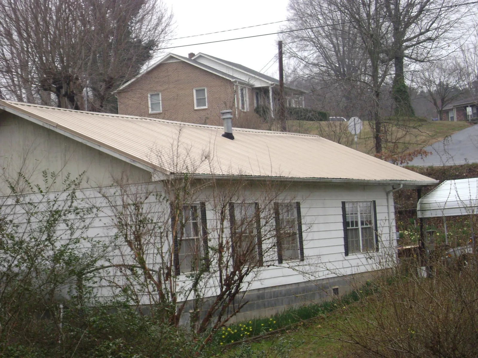 Tan metal roof on a white sided house set into a hillside — Commercial Roofing by Roofing Brothers in Lone Wolf